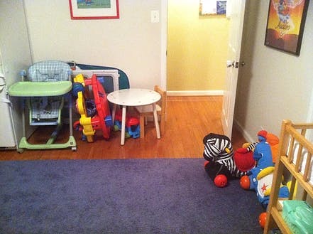Child's high chair, small table, and toys in a room with a rug and wood floor