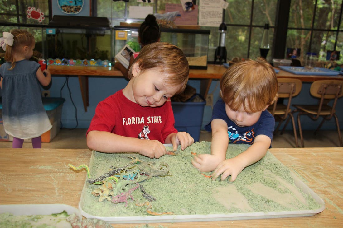Two children playing with sand and toys in a classroom