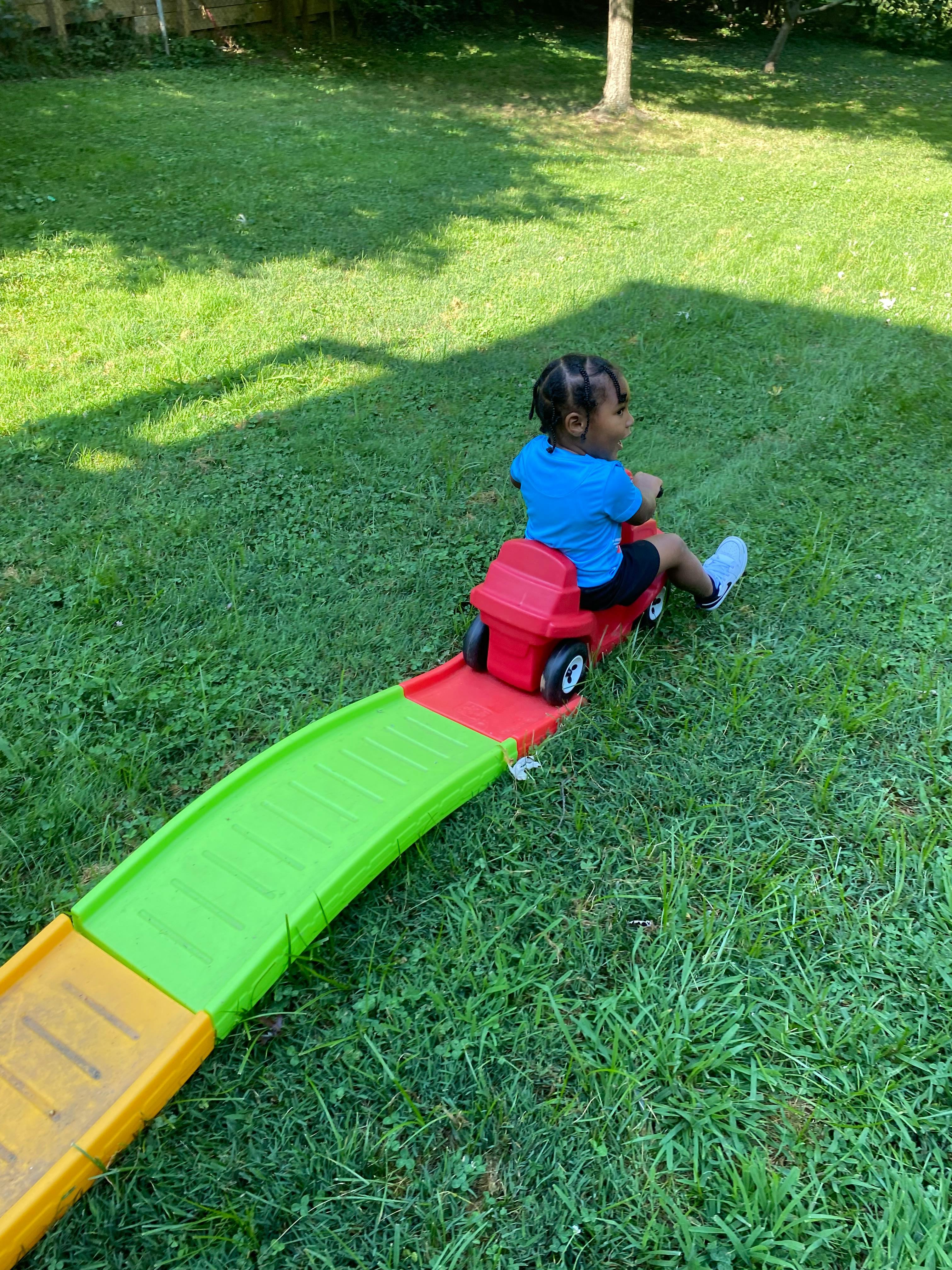 Child on a red toy car on a green and yellow ramp