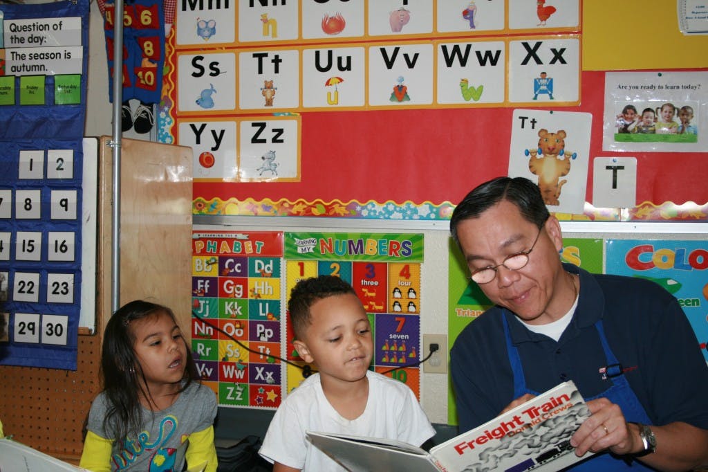 Adult reading a book to two children in a classroom