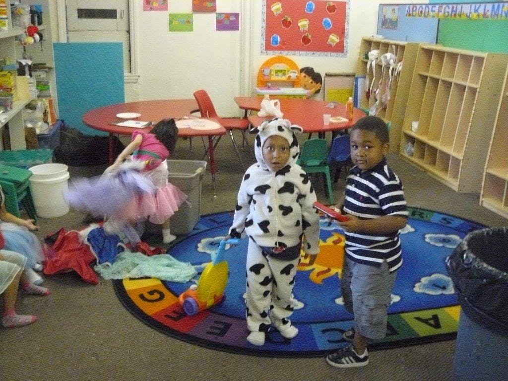 Two children standing on a rug in a classroom, one in a cow costume