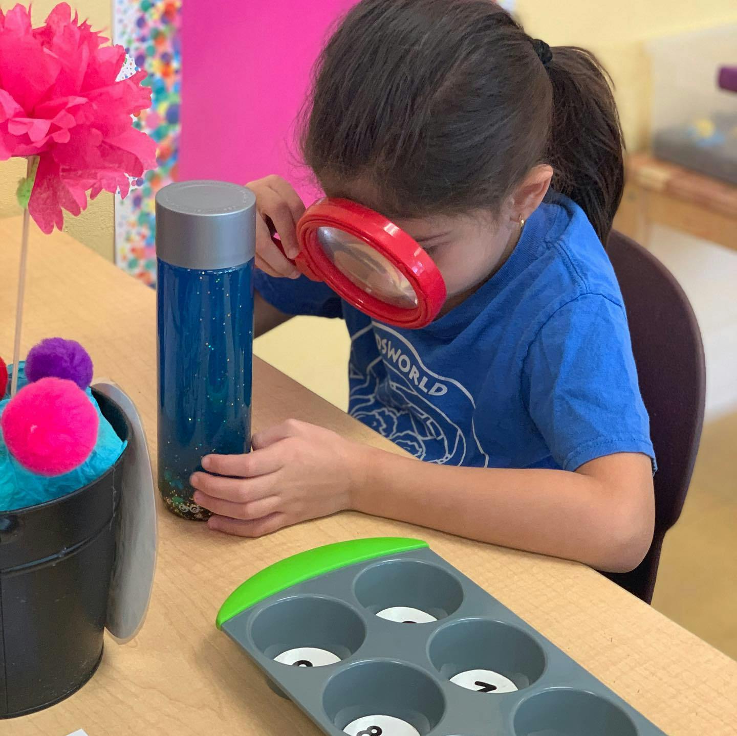 Child looking through a magnifying glass at a blue bottle