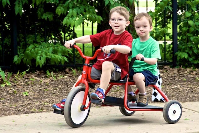 Two children on a red tandem tricycle