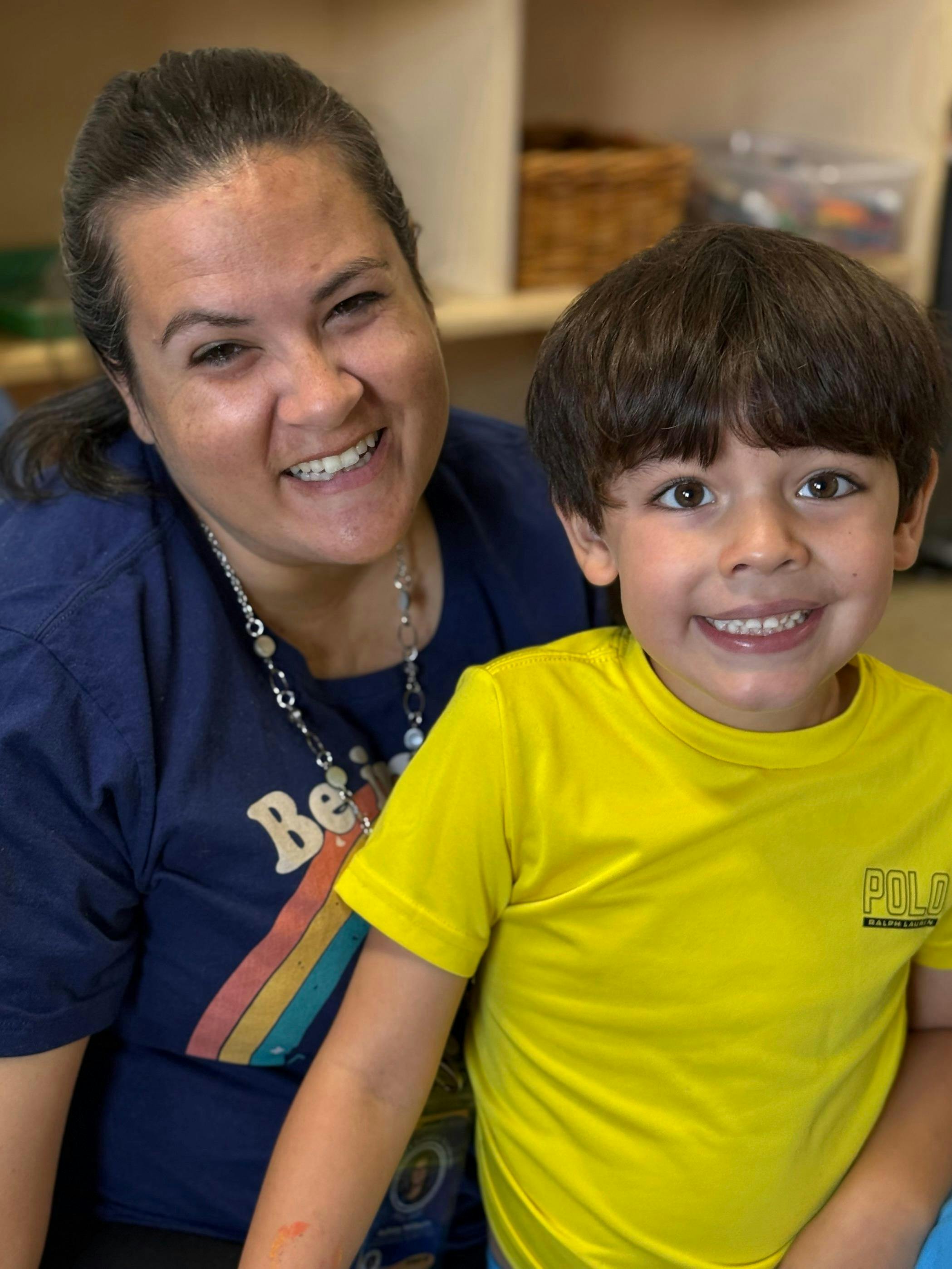 Smiling adult and child with dark hair in a classroom