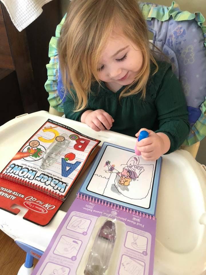Child in a high chair coloring in a book with a blue marker