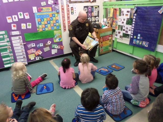 Person in uniform reading a book to children in a classroom