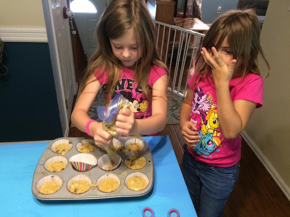 Child filling cupcake liners in a muffin tin, another child standing nearby