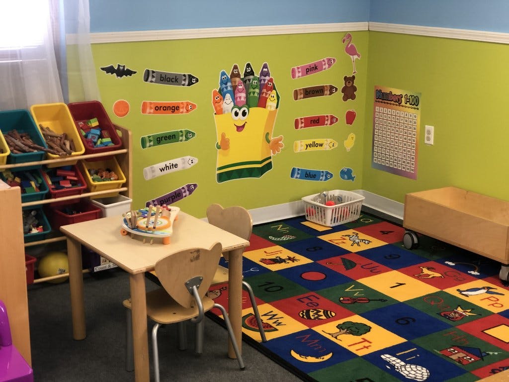 Child's classroom with small table and chairs, toy storage, and alphabet rug