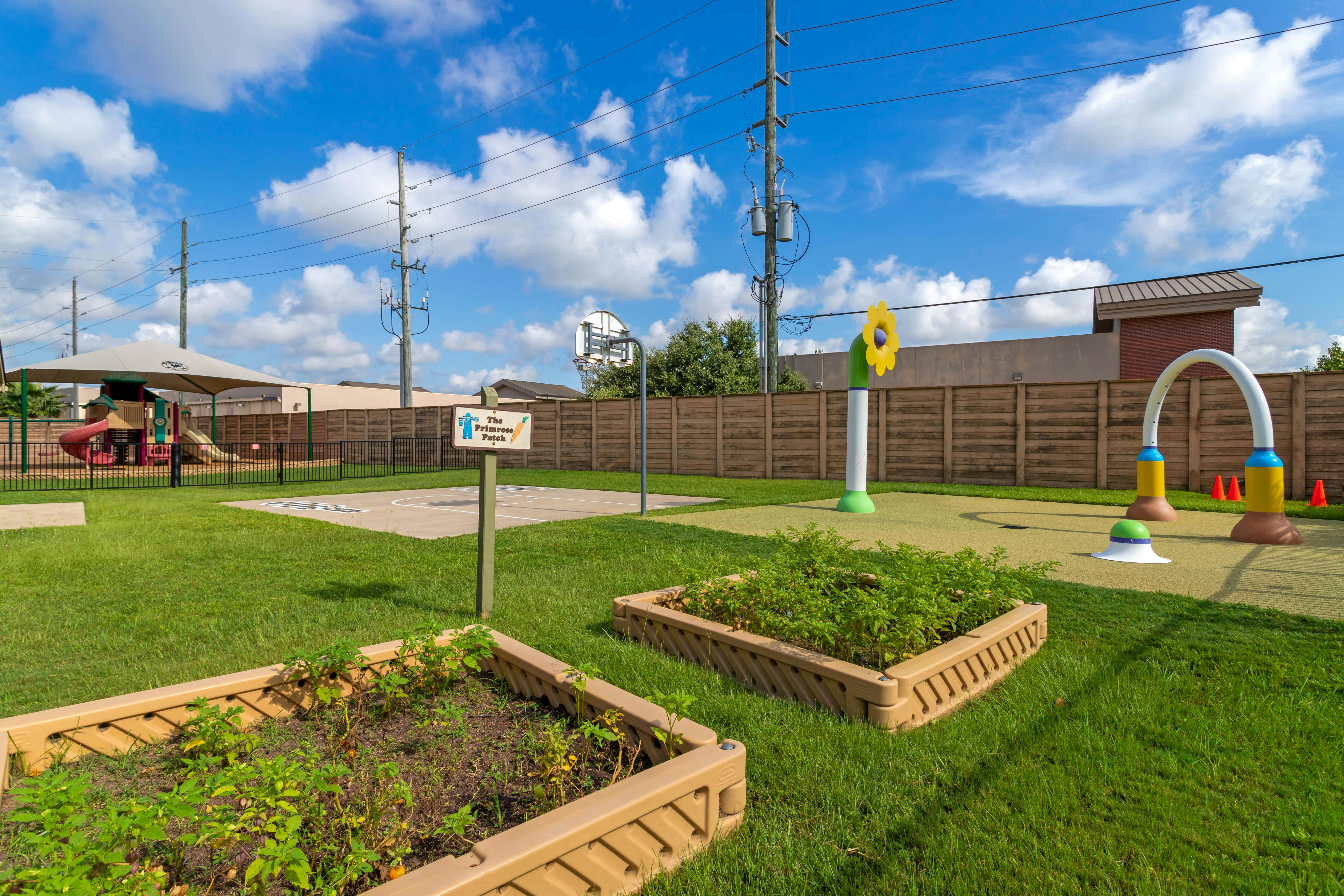 Playground area with climbing structure, basketball court, and splash pad with raised gardens
