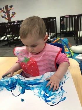 Child in a high chair finger painting with blue paint