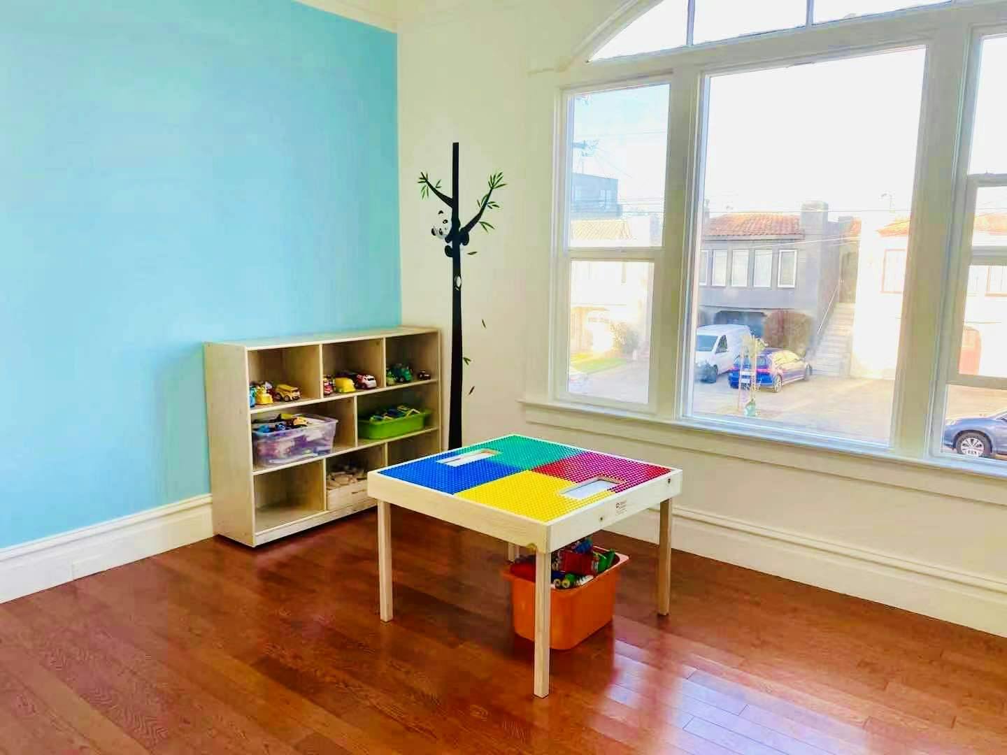 Playroom with a colorful activity table, storage shelf, and large window