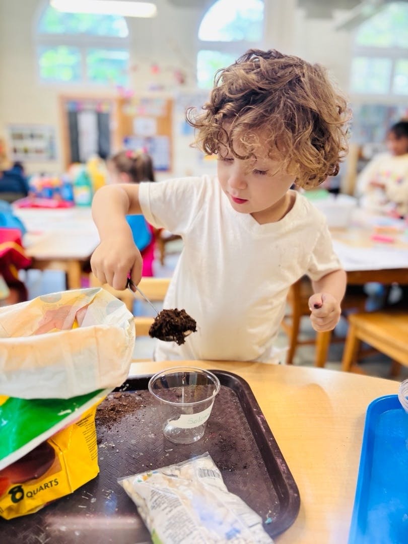 Child placing soil into a small plastic cup in a classroom