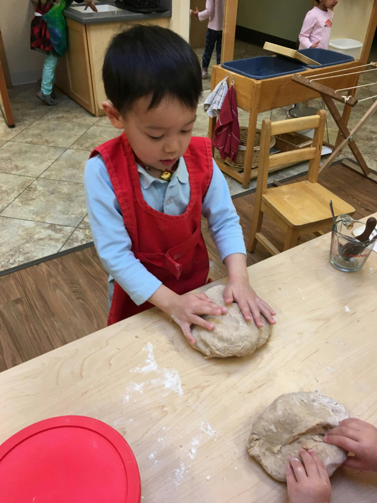 Child in a red apron kneading dough on a wooden table