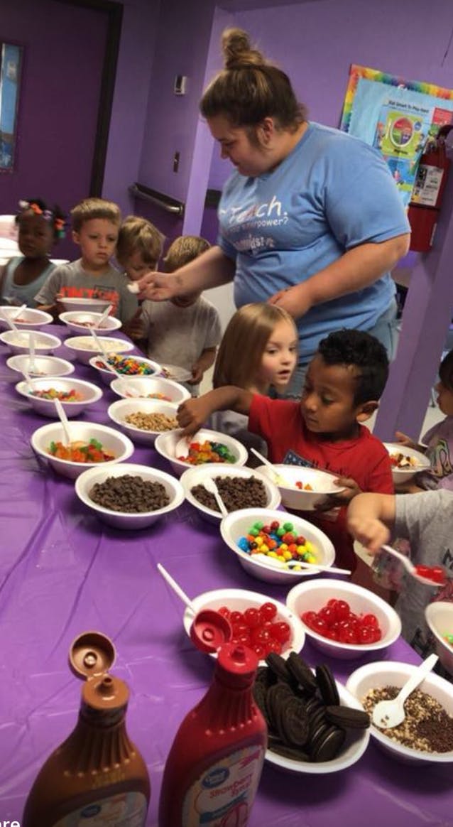 Adult helping children choose toppings from bowls on a table