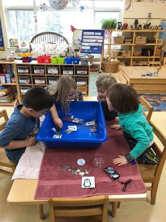 Four children gathered around a blue bin on a table
