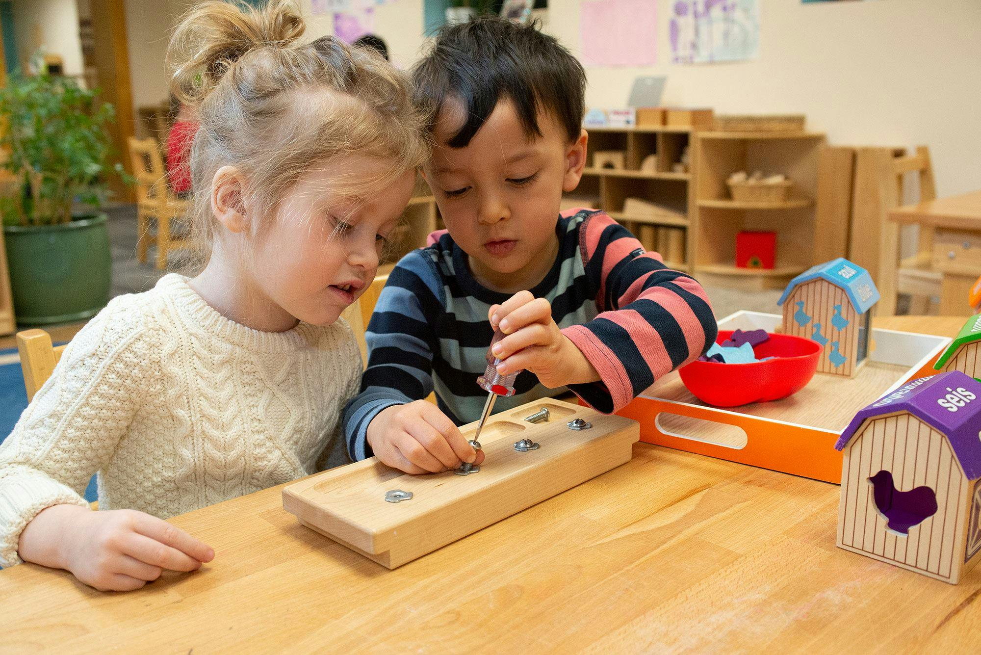 Two children playing with a wooden screw board in a classroom