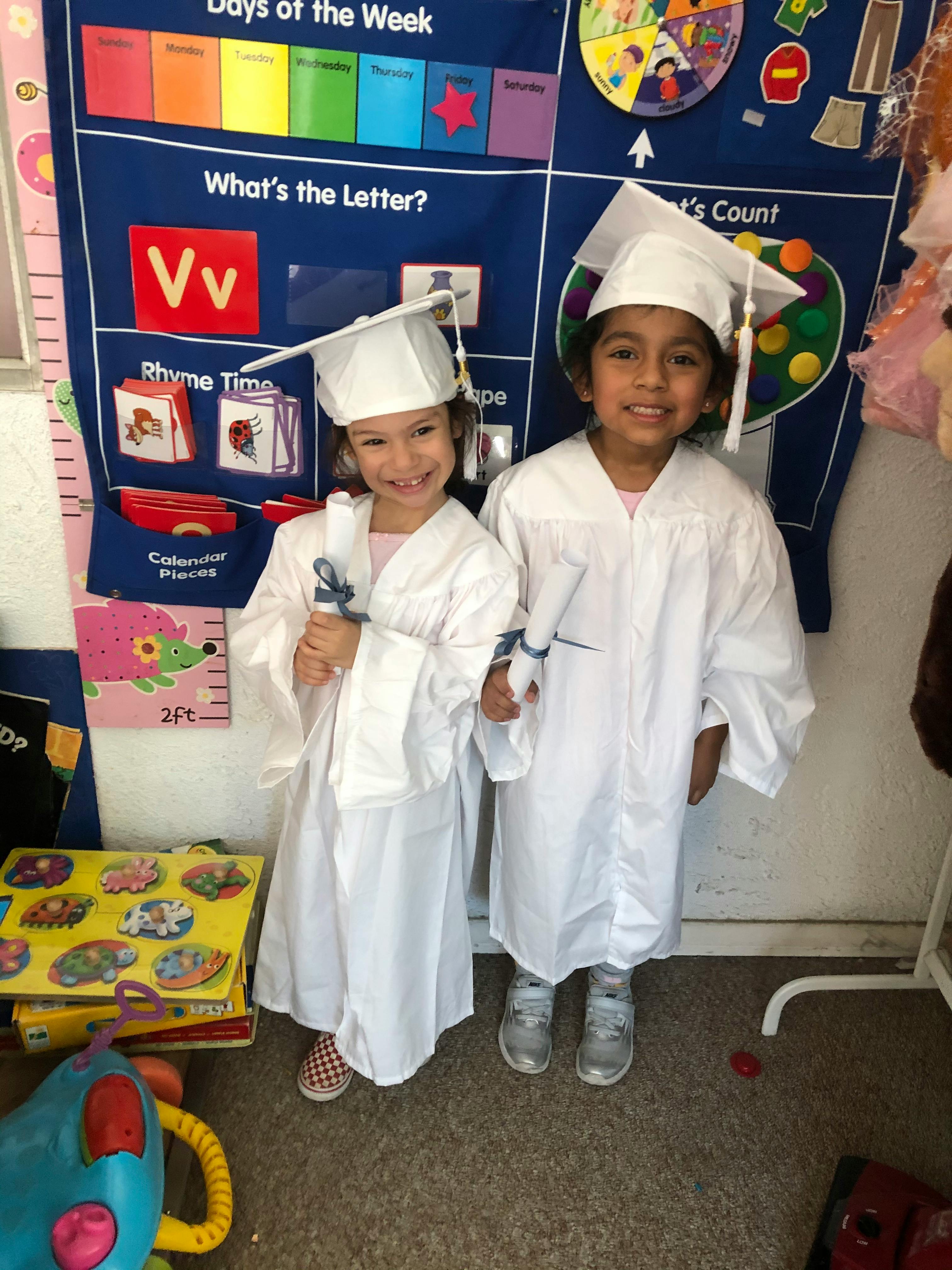 Two children in graduation caps and gowns holding diplomas