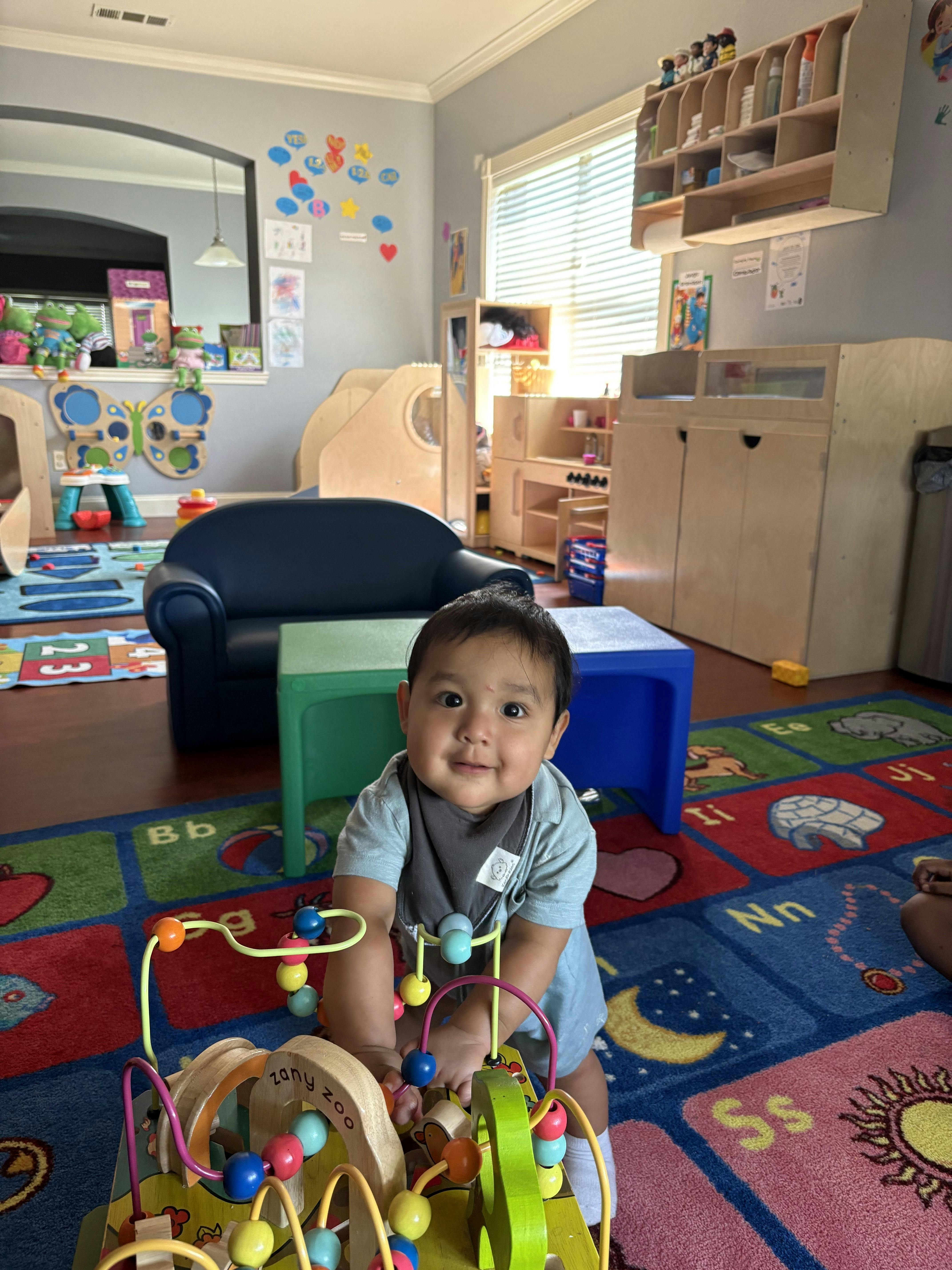 Child playing with a bead maze toy on a colorful alphabet rug in a playroom