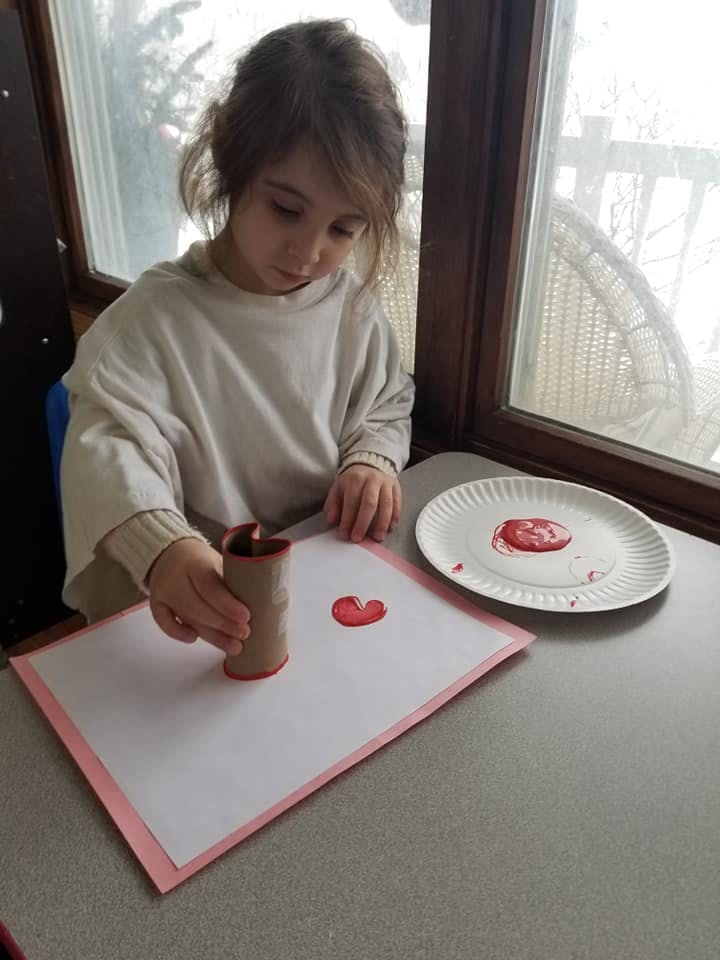 Child making a heart shape print with a cardboard tube and red paint