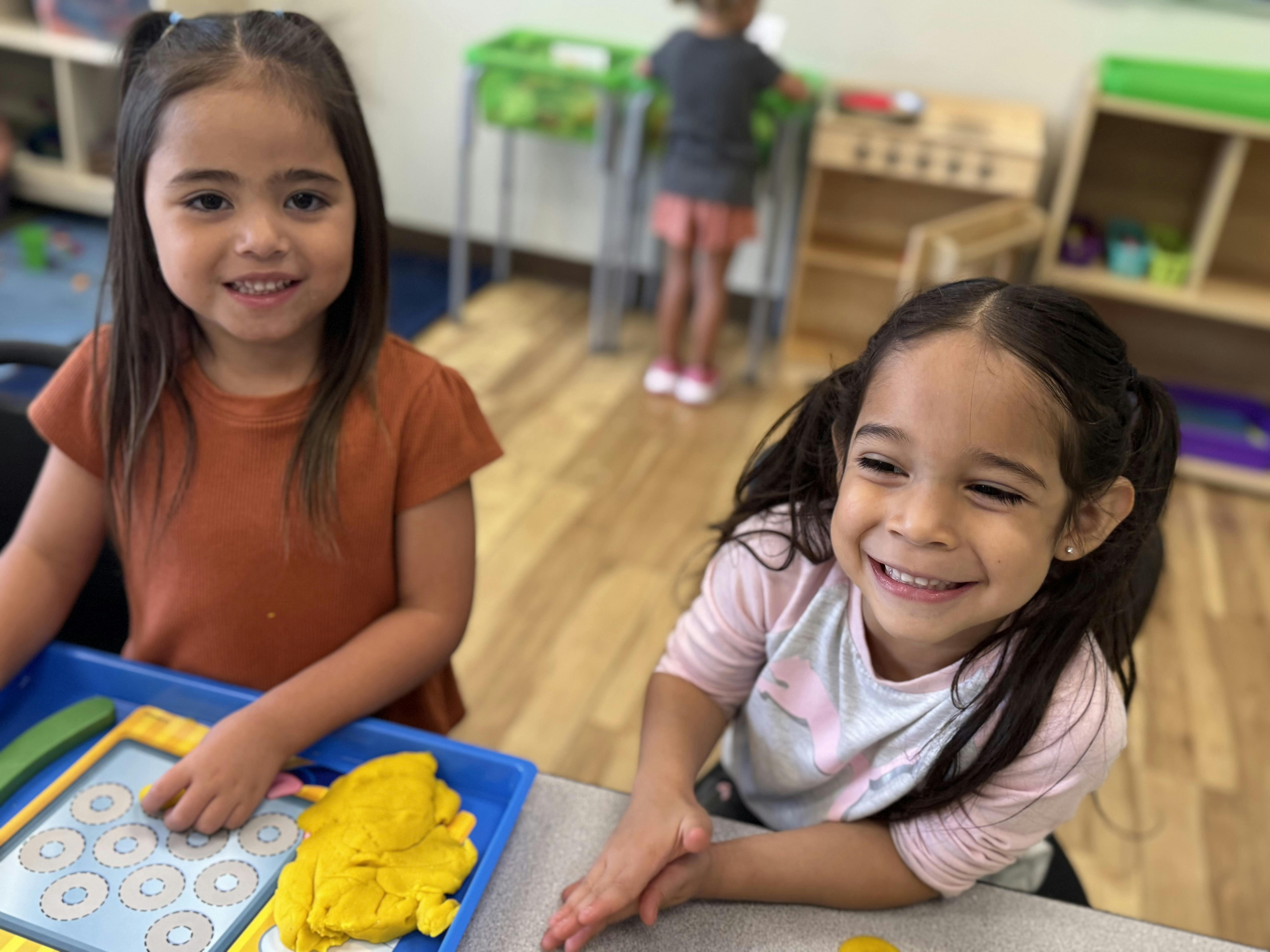 Two children at a table, one playing with yellow playdough