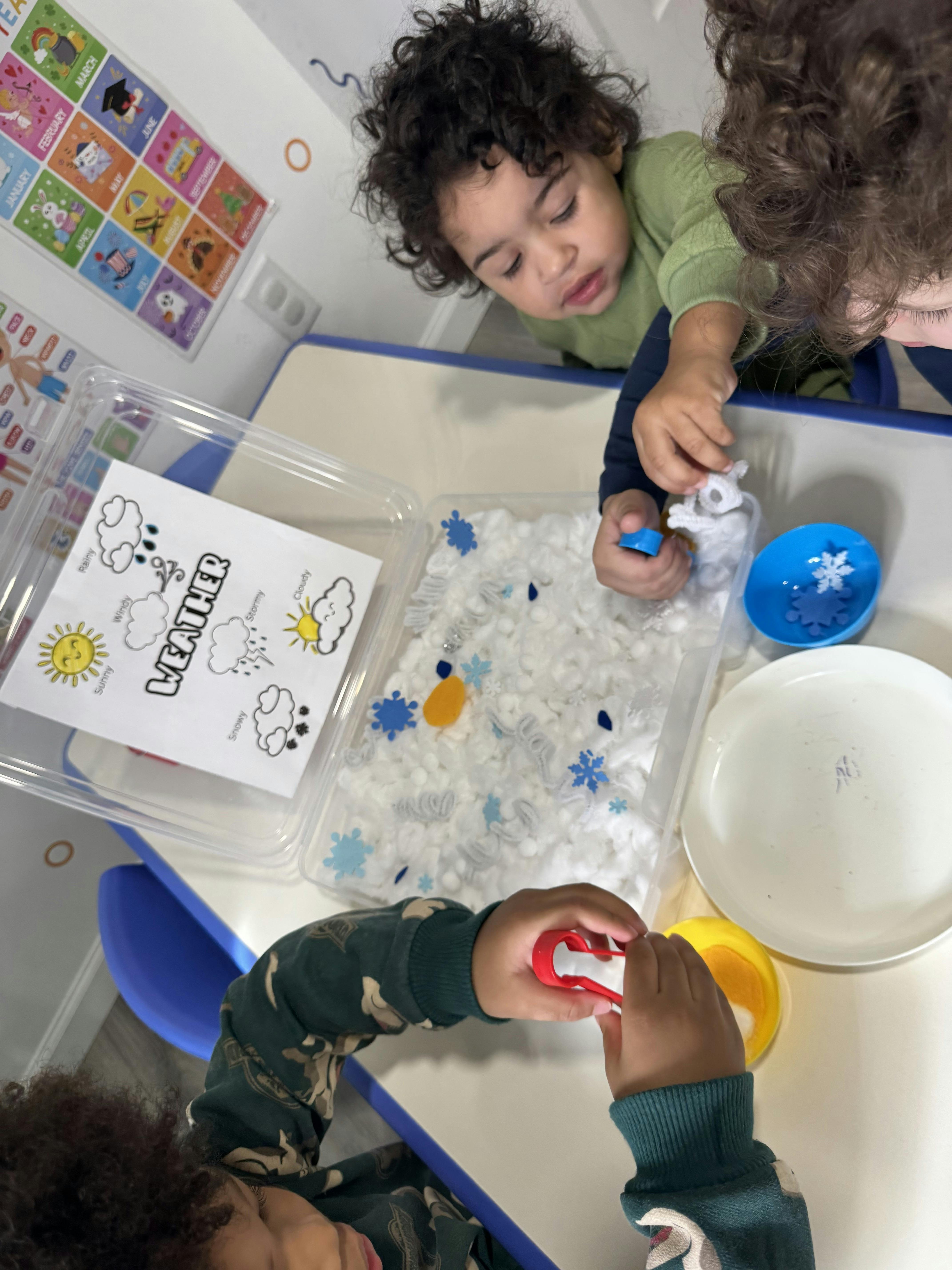 Two children playing with cotton balls, snowflakes, and small toys on a table