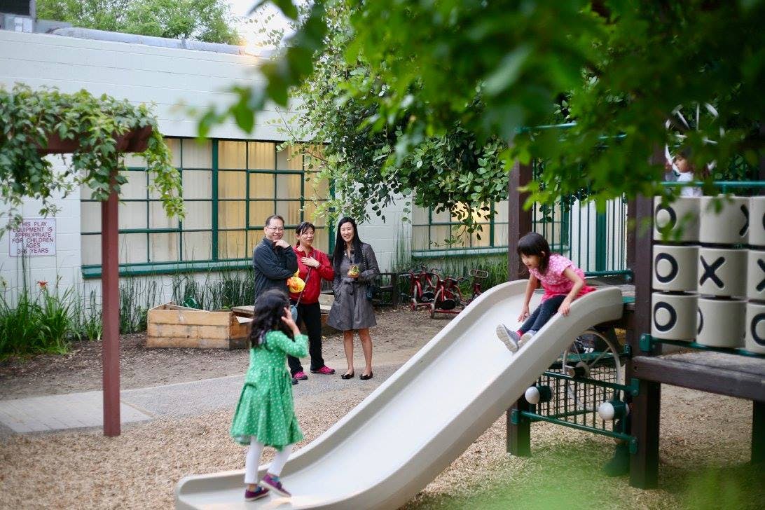 Children playing on a slide in a playground with adults nearby