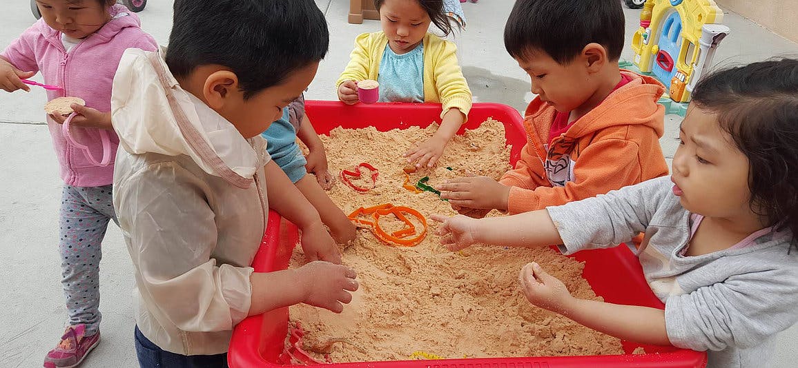 Children playing with kinetic sand in a red bin