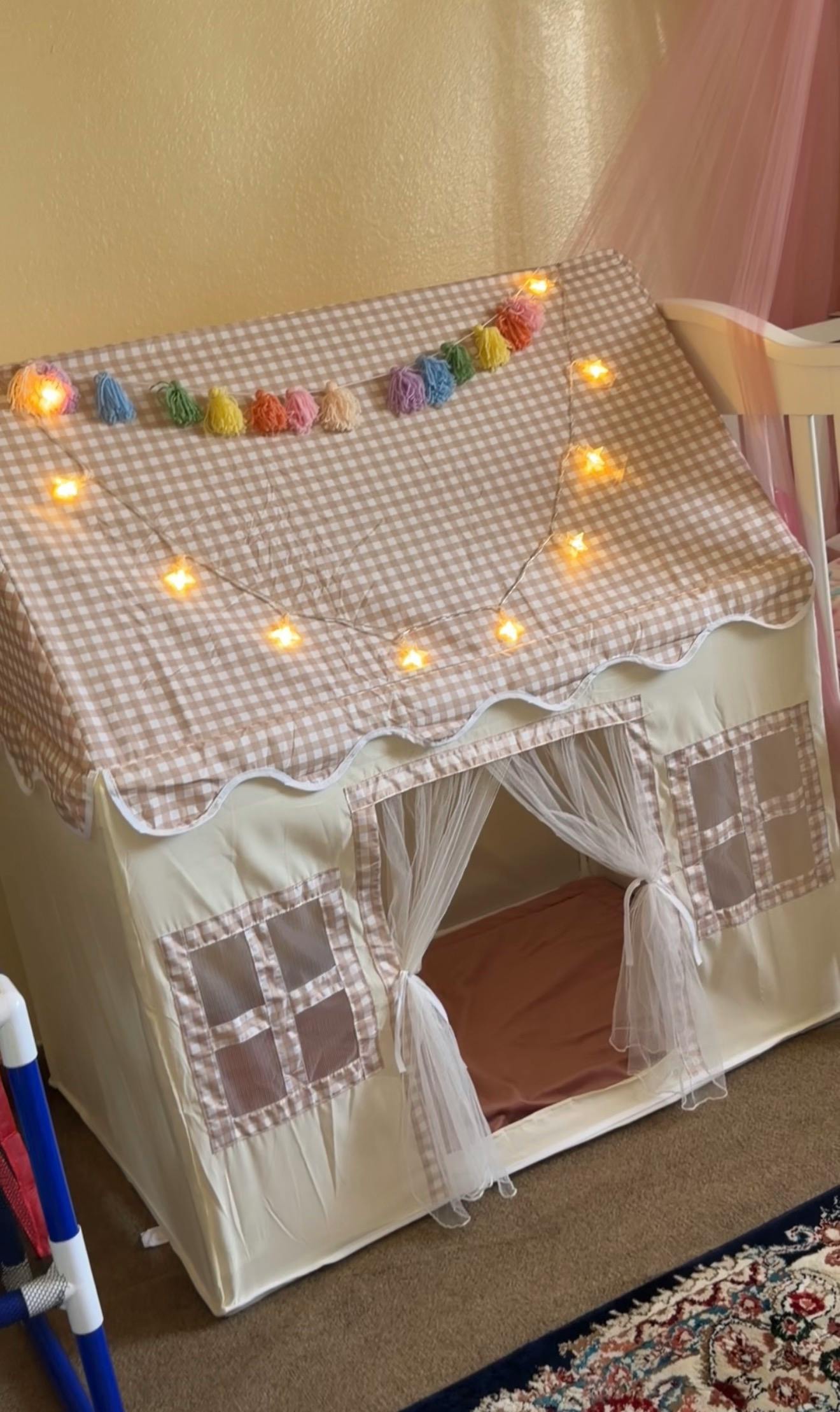 A beige fabric play tent with a checkered roof decorated with star lights