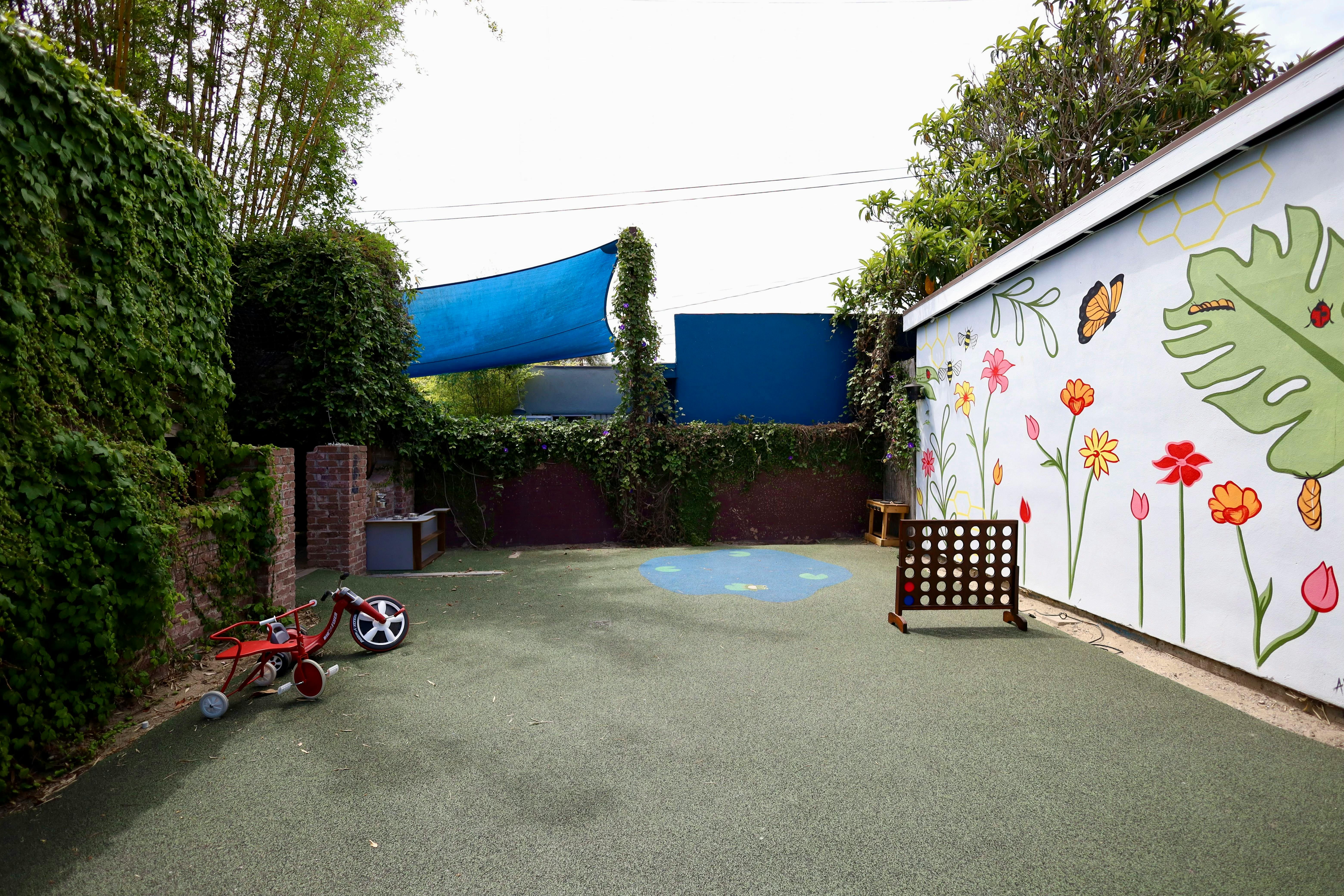 An outdoor play area with artificial turf, a mural, and a red tricycle