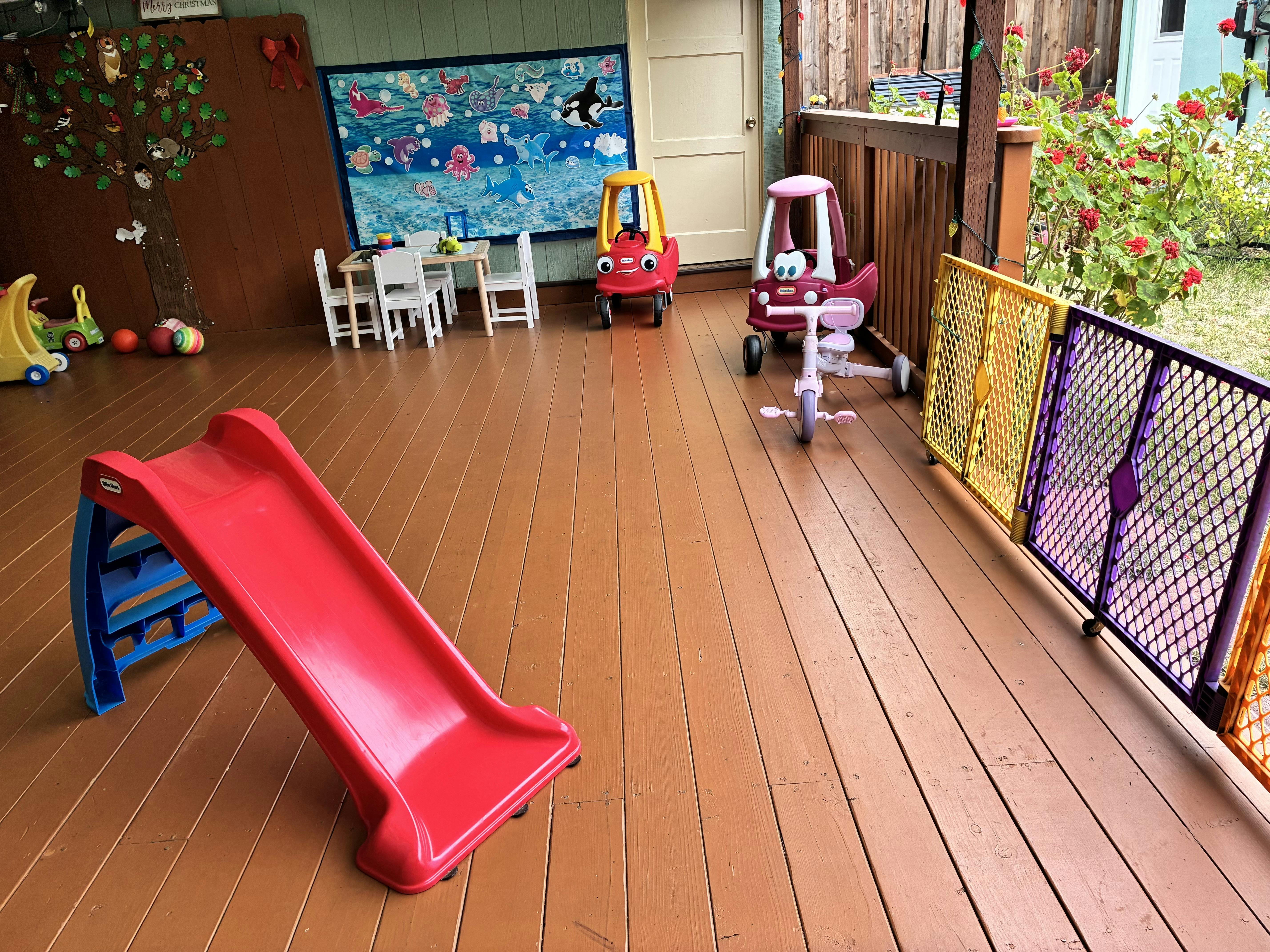 Play area on a wooden deck with a small slide, ride-on cars, and a table