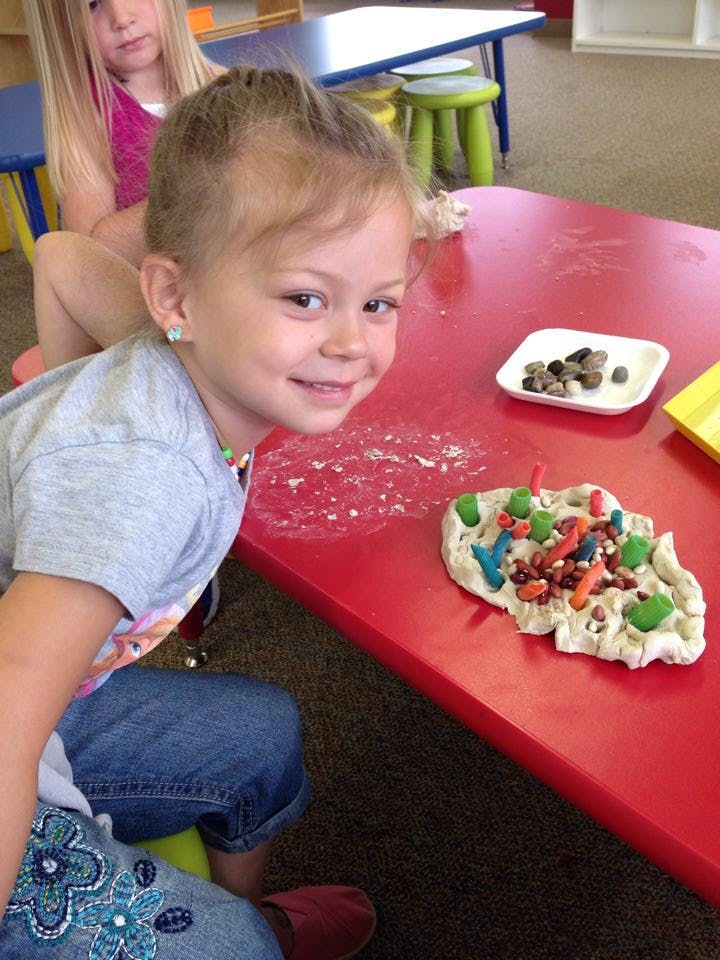 Child at a red table with playdough and small objects