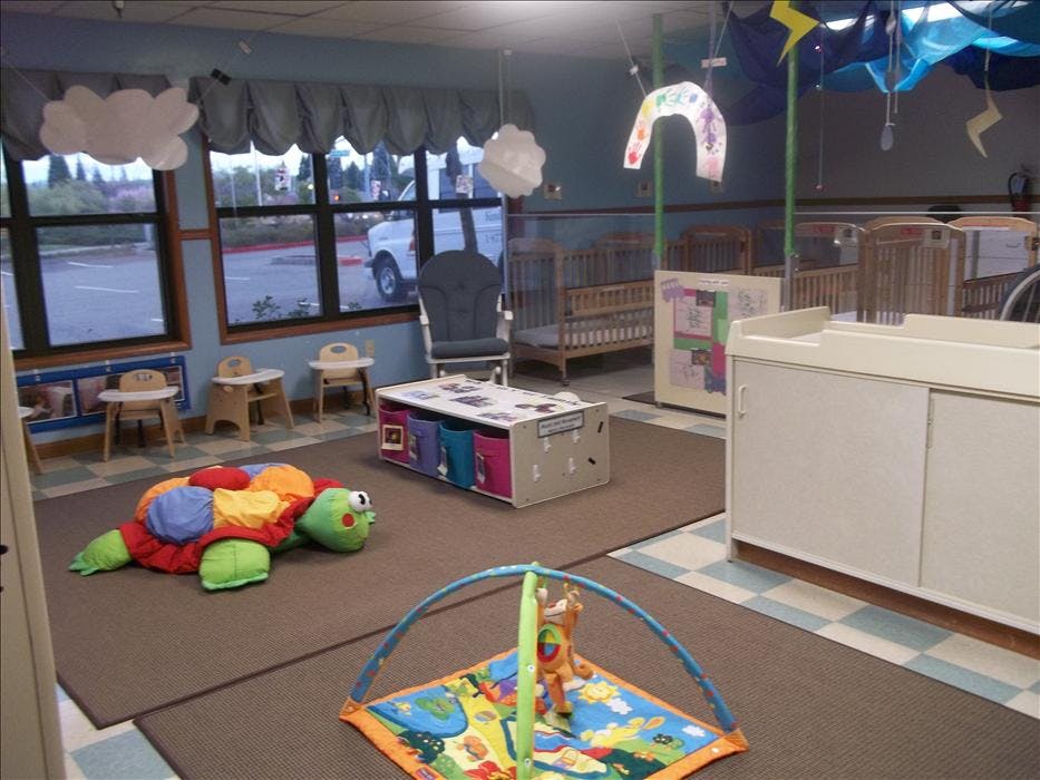 Childcare room with cribs, play mat, changing table, and stuffed turtle