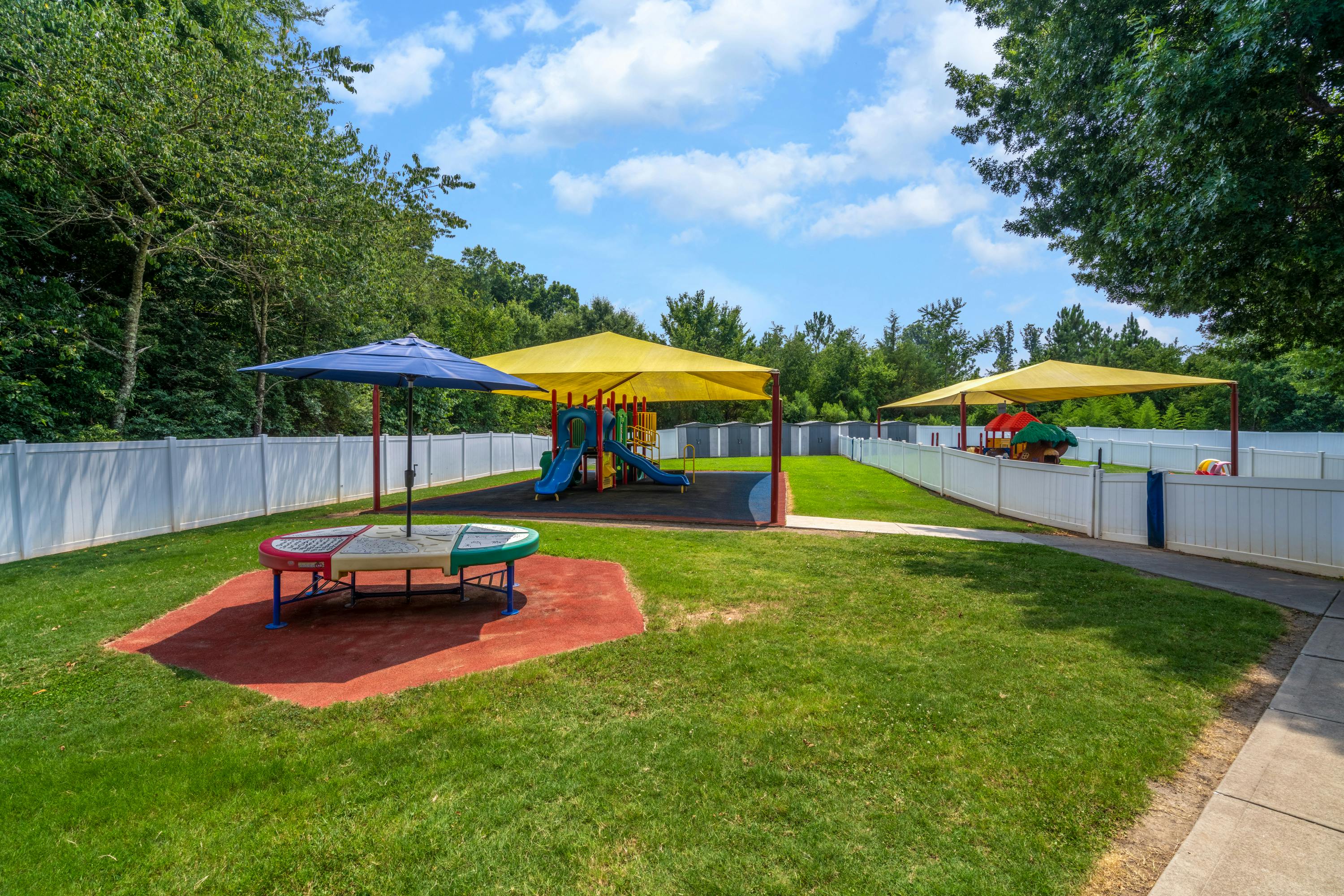 Outdoor playground with play structures under yellow canopies and a blue umbrella
