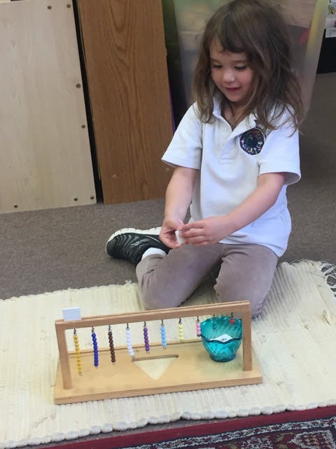 Child kneeling on a rug, playing with a wooden bead frame