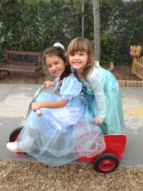 Two children in light blue dresses on a red toy wagon