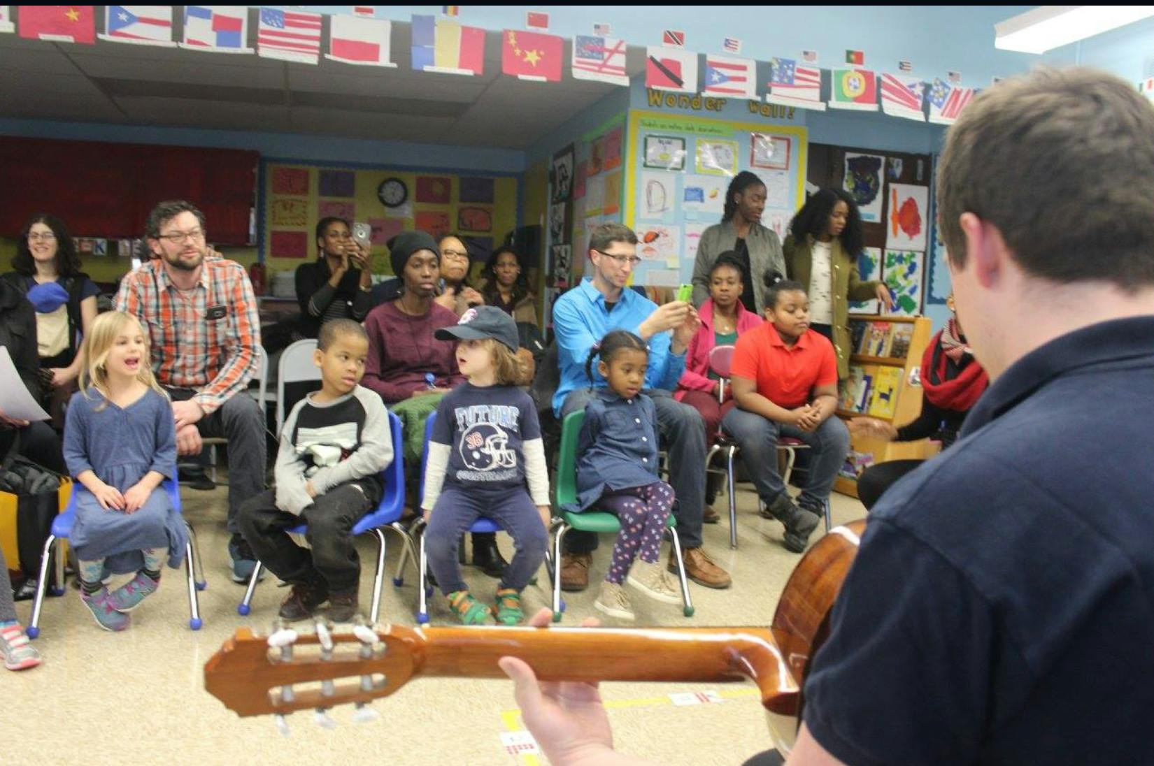 Person playing guitar for a group of adults and children in a classroom