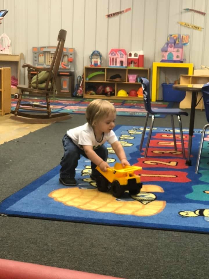 Child playing with a toy truck on a colorful rug in a classroom