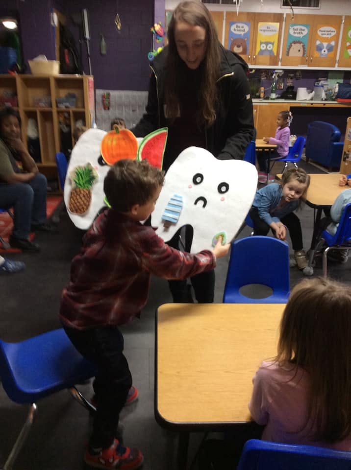 Adult and child holding large tooth and fruit cutouts in a classroom