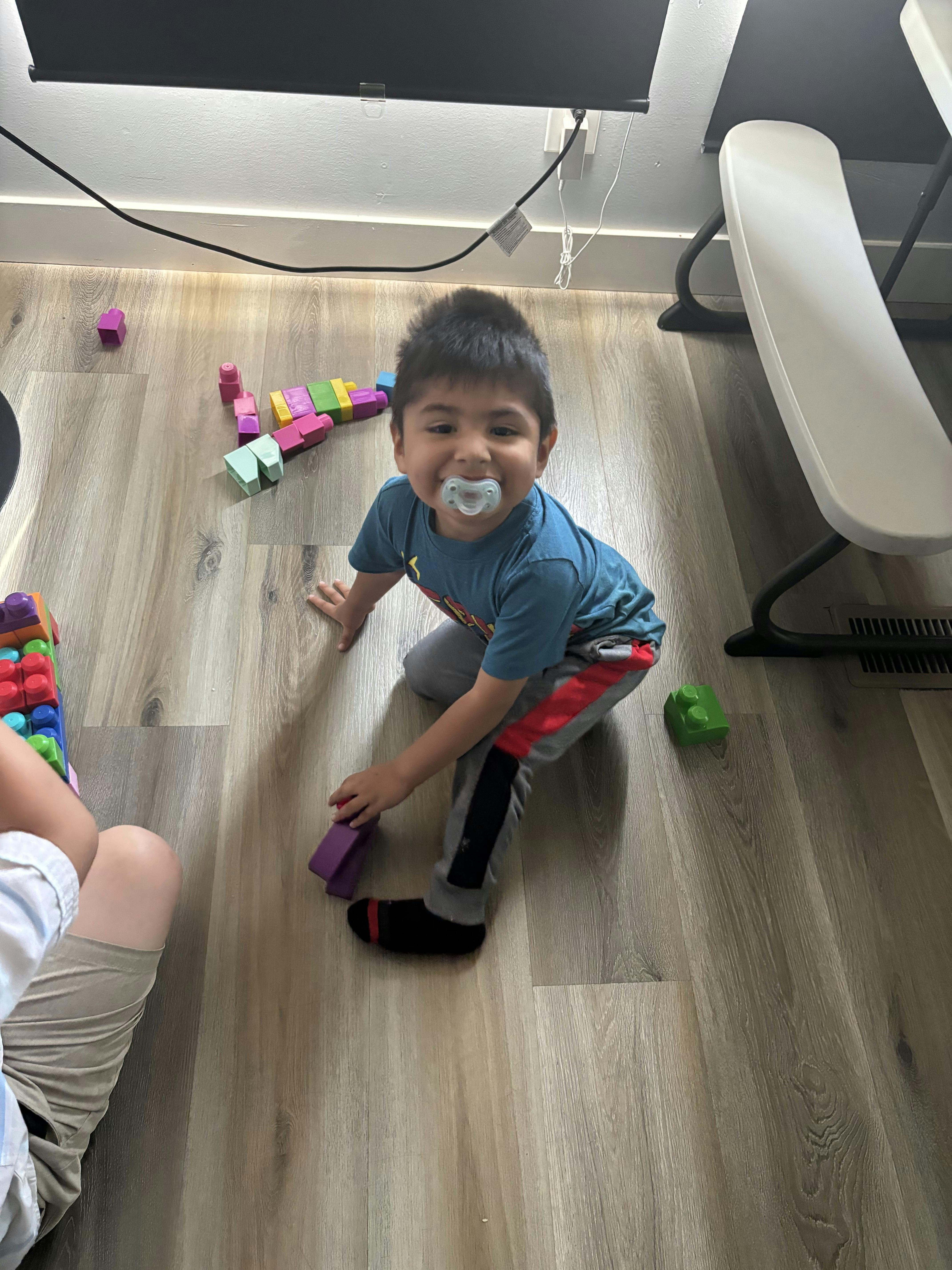 Child with pacifier on floor playing with blocks