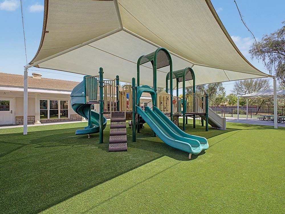 Playground with green slides and a large shade canopy over artificial turf
