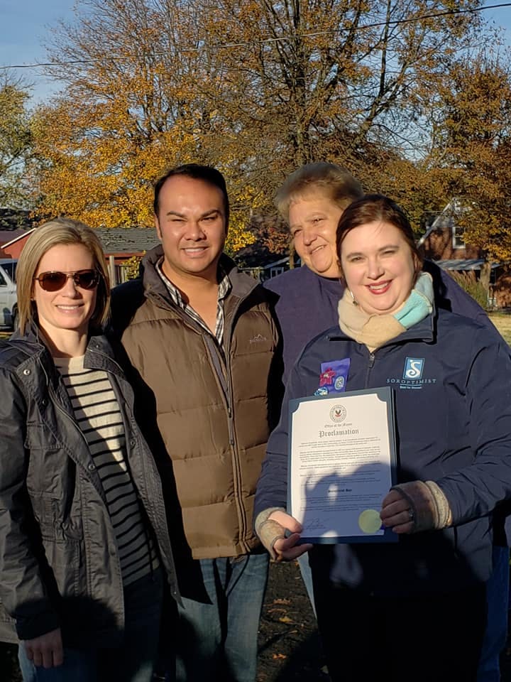 Four people standing outdoors, one holding a document