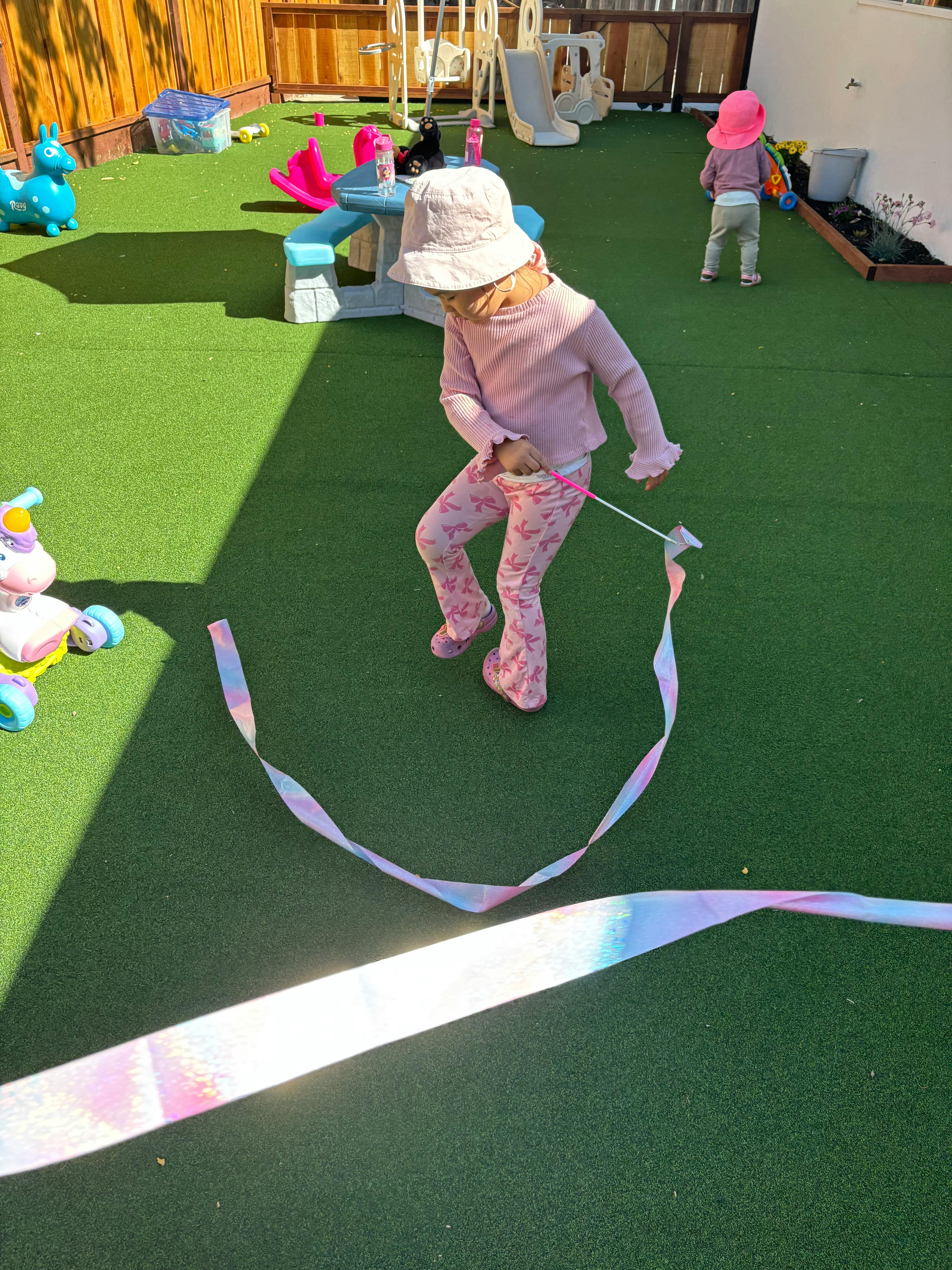 Child in a hat playing with a ribbon on artificial grass