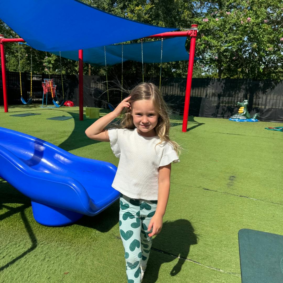 Child standing on playground with hand near head