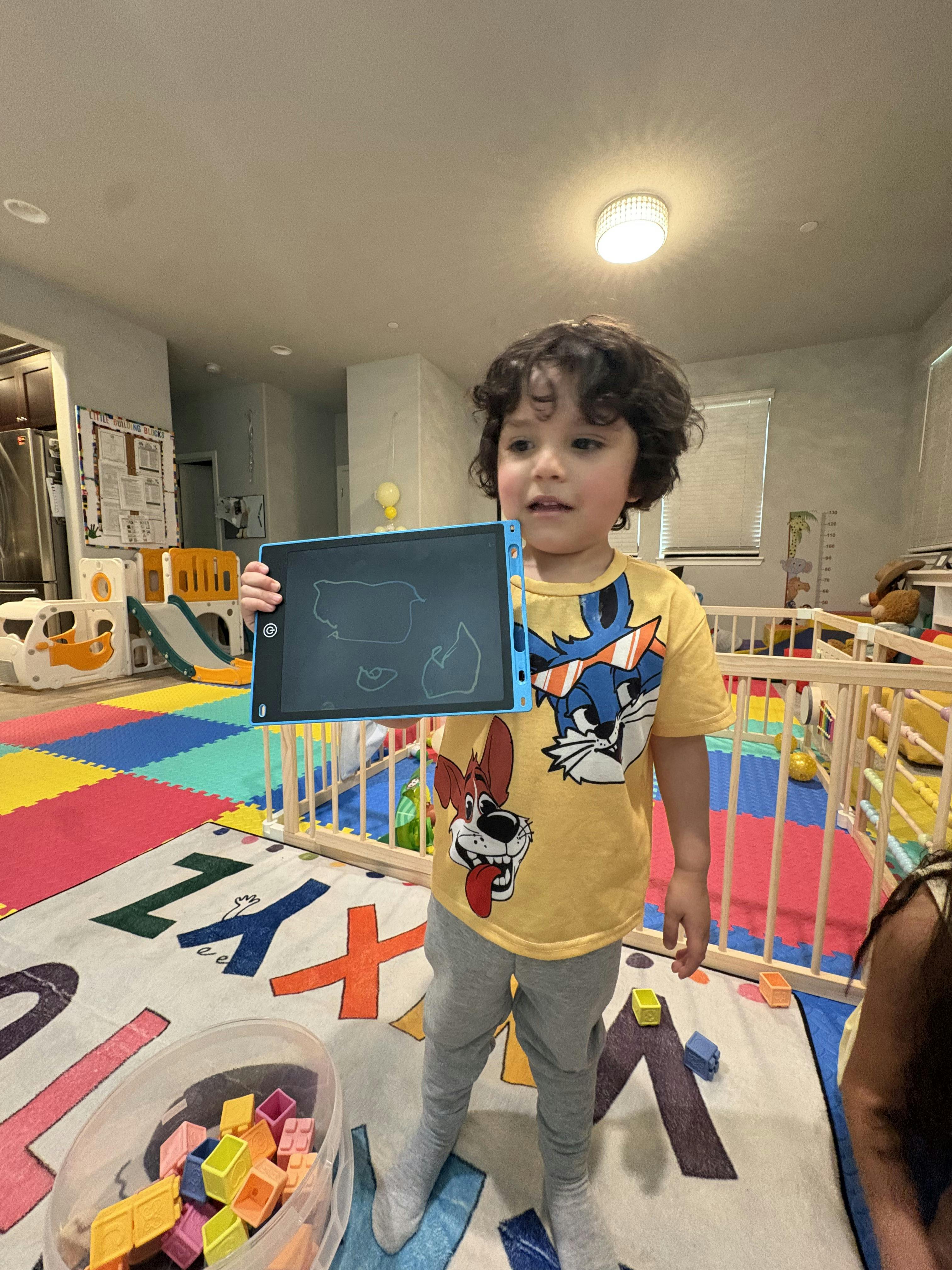 Child in a yellow shirt holding up a blue drawing tablet