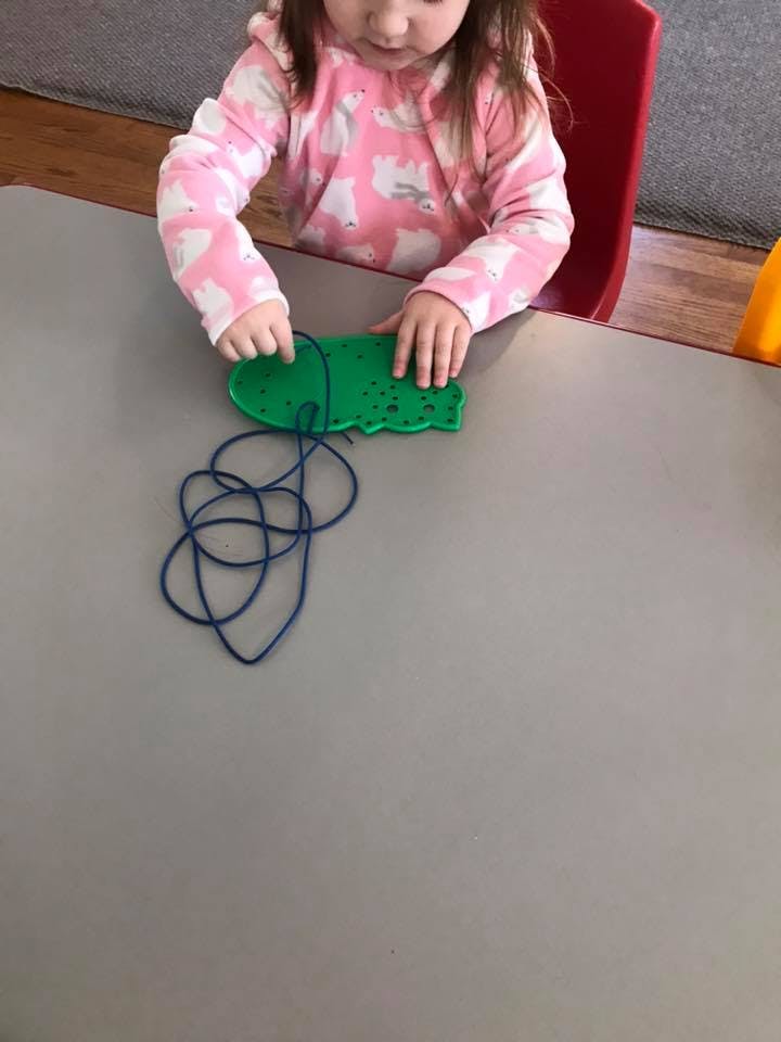Child lacing a green shape with blue string