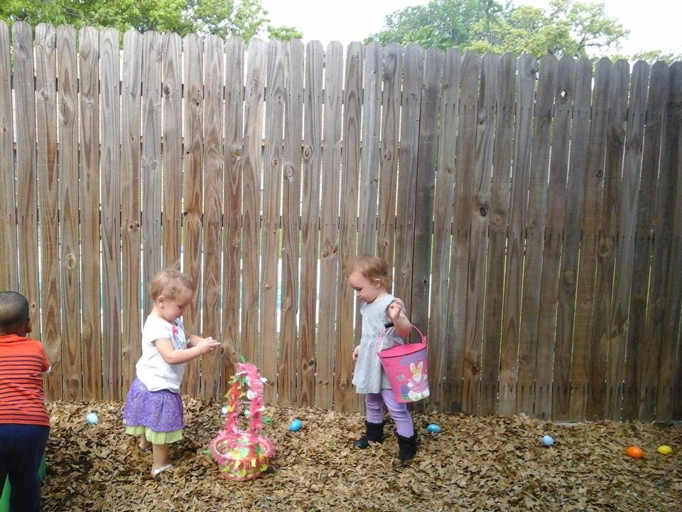 Two children playing with an Easter basket and eggs near a wooden fence