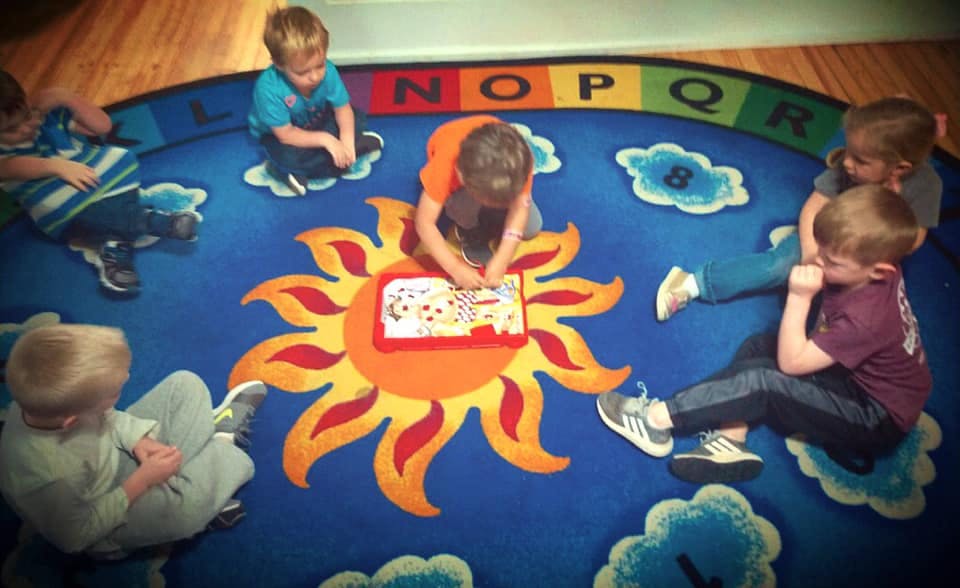 Children sitting on a rug with one child drawing