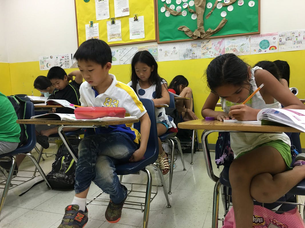 Children sitting at desks in a classroom, writing and reading