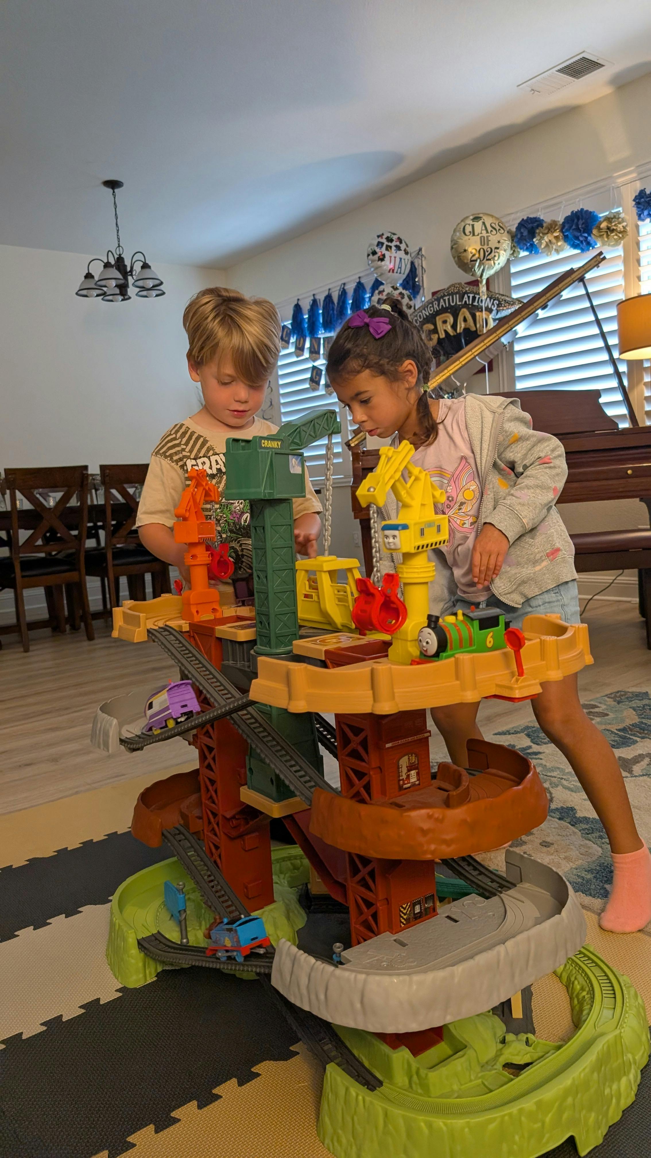 Two children playing with a multi-level toy train set