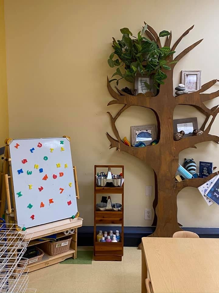 Whiteboard with colorful magnetic letters next to a tree-shaped bookshelf